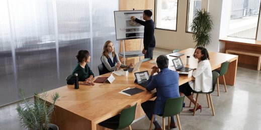 Fünf Personen in einem Meetingraum, ein Mann macht Notizen auf Surface Hub