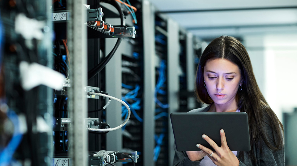 Junge Frau steht mit Tablet in einem Serverraum