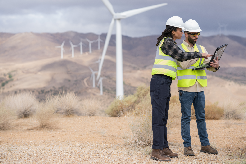 Zwei Techniker*innen diskutieren Daten, die nach der Inspektion von Turbinen in einem Windpark auf einem Laptop angezeigt werden.