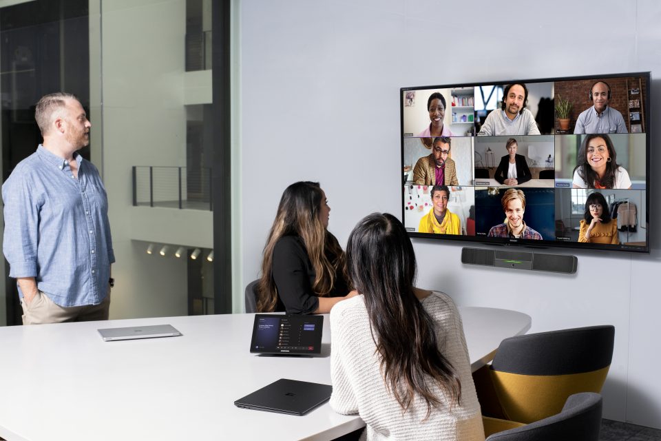 Personas en una sala de juntas observan una videollamada en un monitor