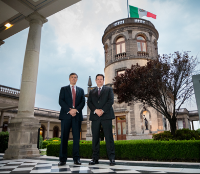 Dos hombres posan con la bandera de México detrás