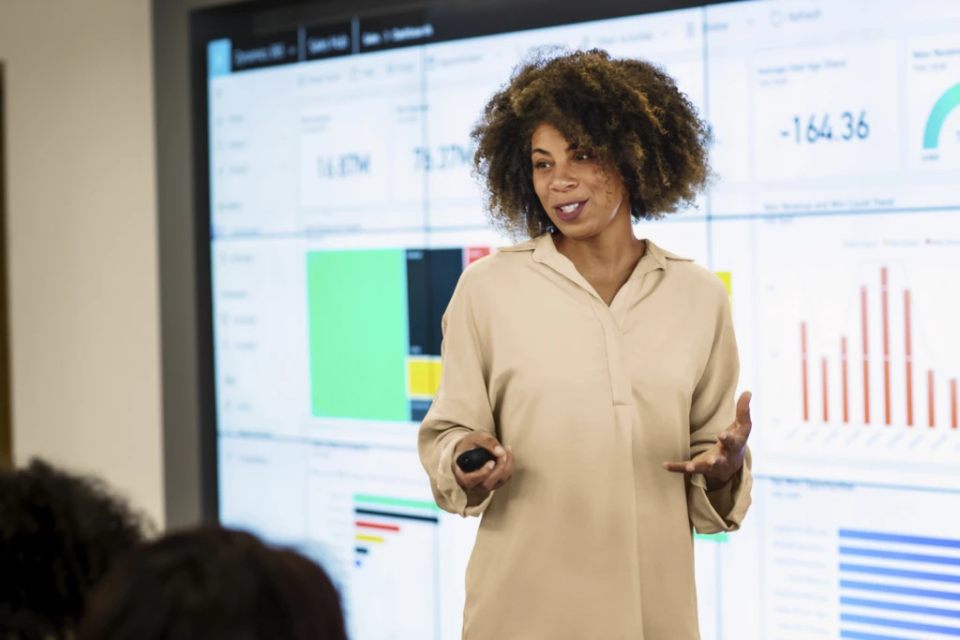 Mulher faz apresentação diante de uma tela de Power BI.