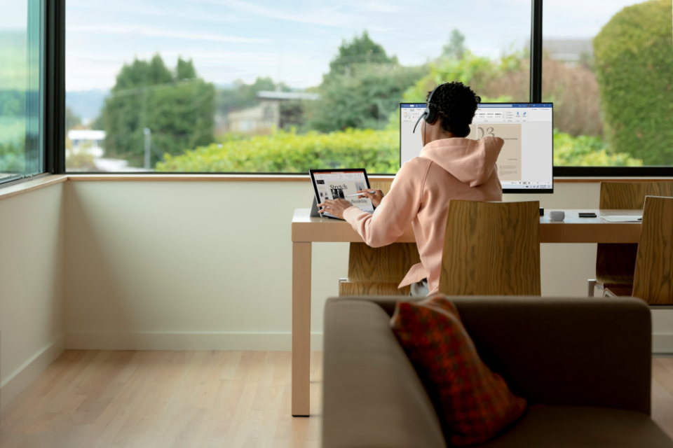 sala de estar com vista para jardim e menino em mesa usando pc e notebook