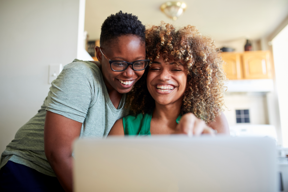 duas mulheres sorrindo e se abraçando olhando um note
