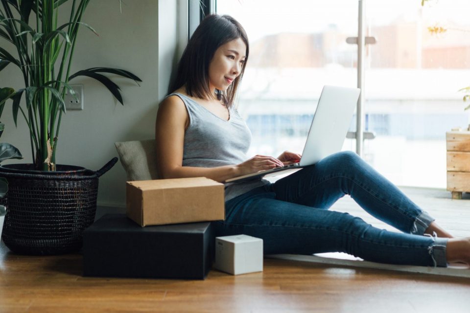 Mulher sentada digita em notebook que está em seu colo.