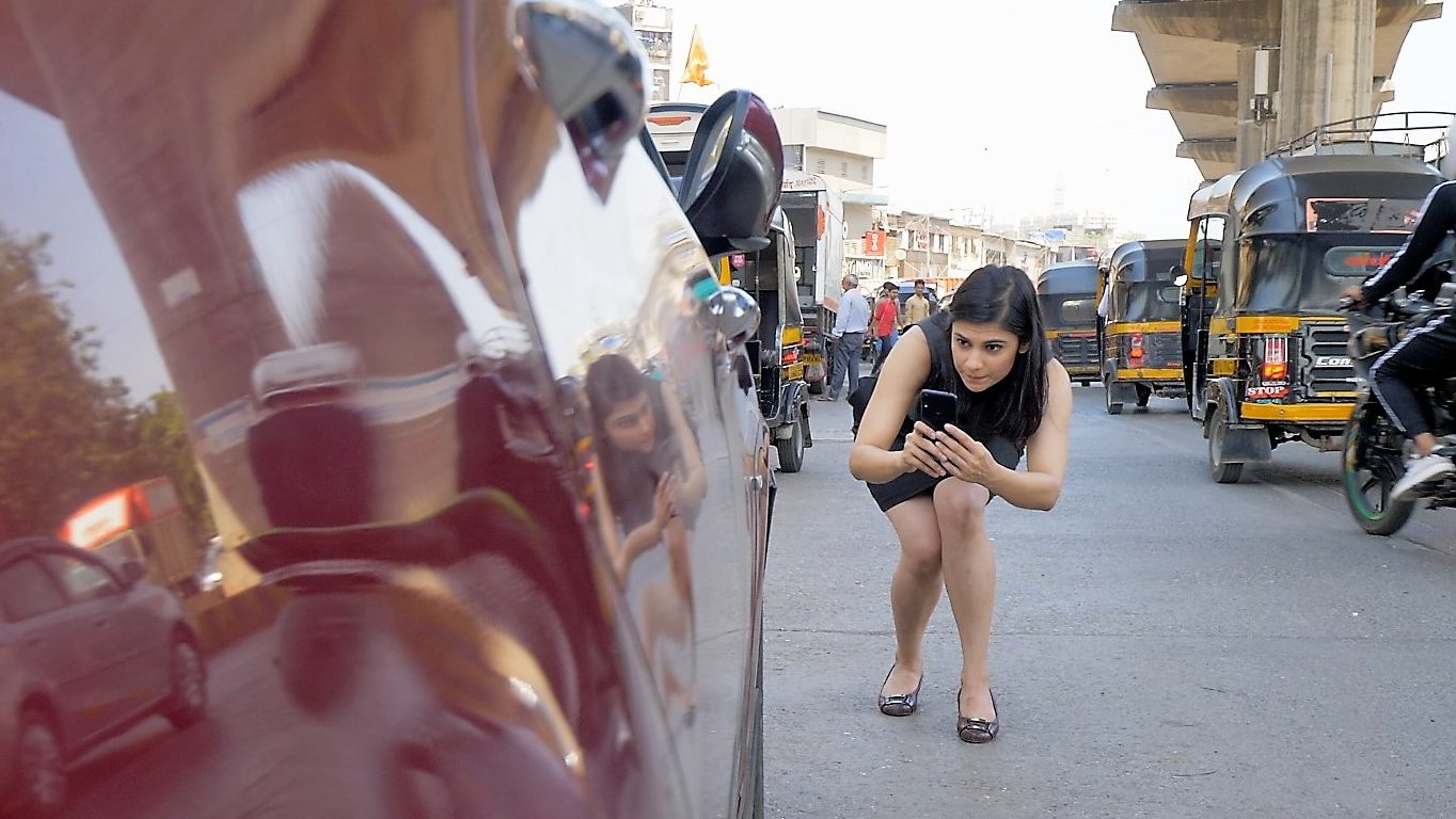 Woman takes a smartphone image of her damaged car on a busy street