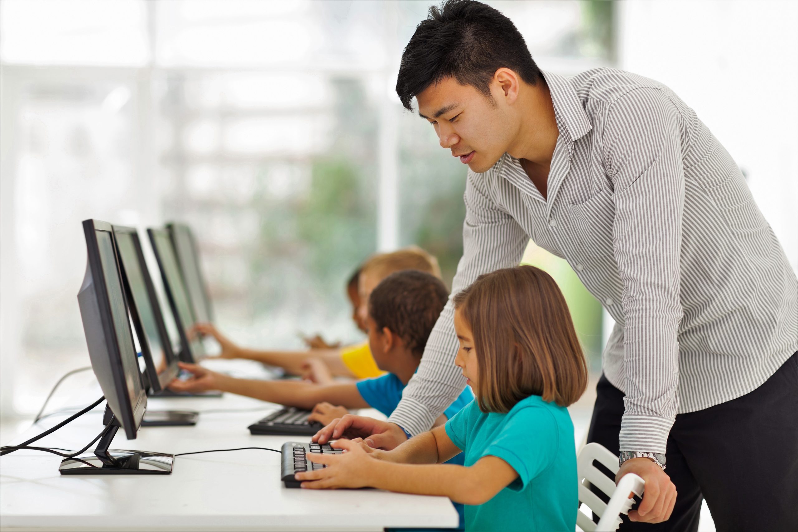 A teacher watches over a row of students using computers