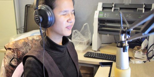 A woman wearing headphones and taliing into a microphone.