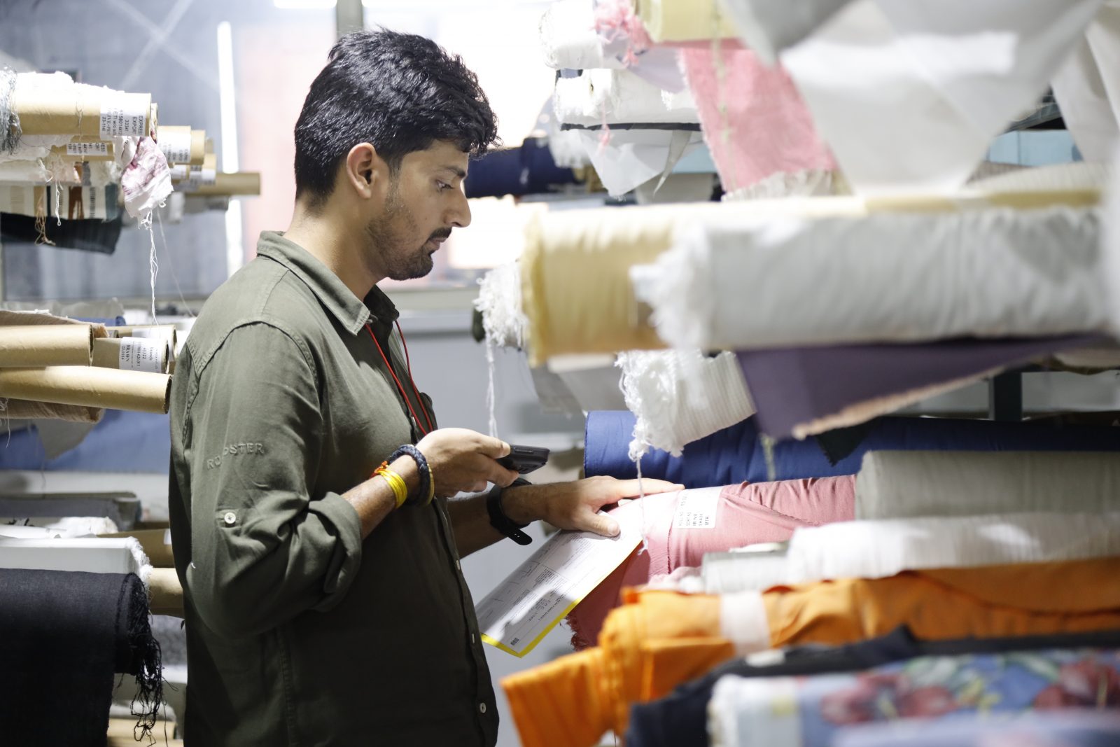 Photo of a man pointing a phone scanner at a label on a roll of fabric stacked in a shelf