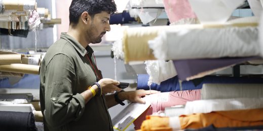 Photo of a man pointing a phone scanner at a label on a roll of fabric stacked in a shelf