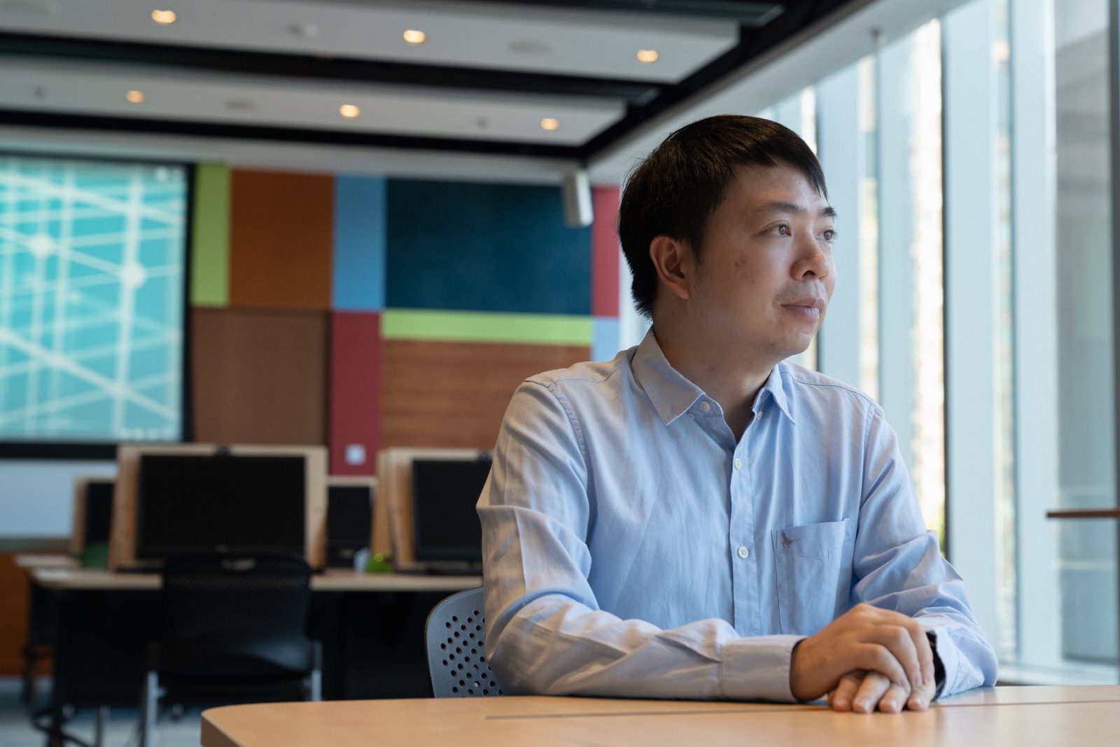 Photo of a man sitting at a table in an office, looking out the window