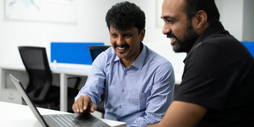 Photo of two men sitting at a desk looking at a computer