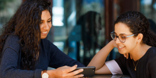 Two women smiling while looking at the mobile screen