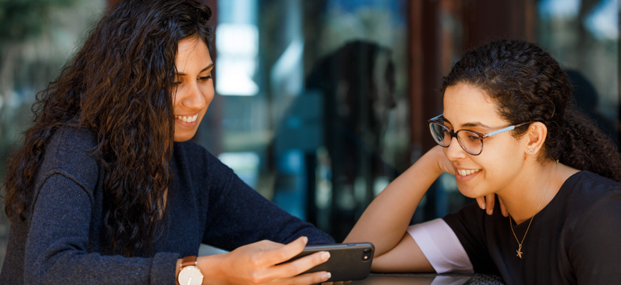 Two women smiling while looking at the mobile screen