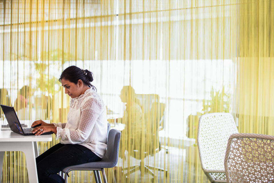 A female employee works on her laptop while sitting in common space in office