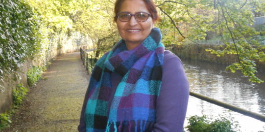 a woman smiling at the camera with a canal and foliage in the background