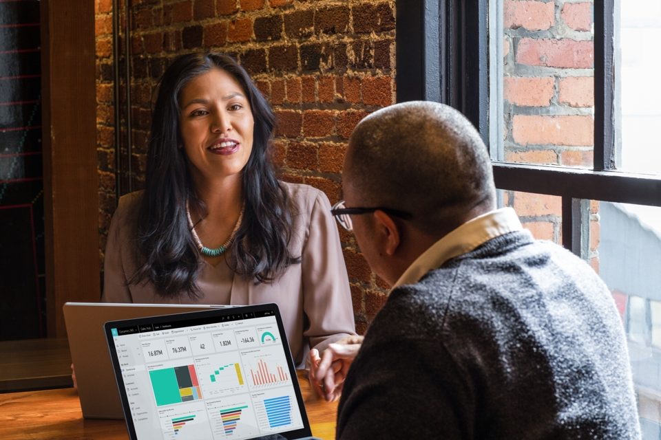 A photo of a woman in discussions with a man sitting in front of a laptop