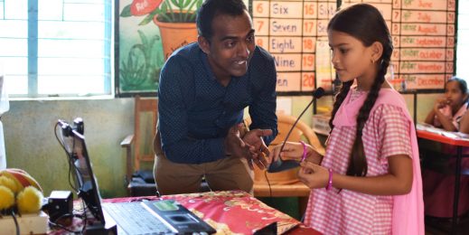 A photo of a male teacher teaching a girl in uniform using technology