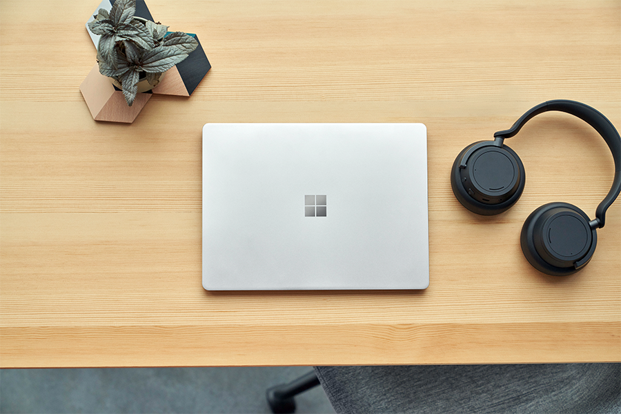 a photo of surface laptop go 2 lying on a table with a pair of headphones and a pot