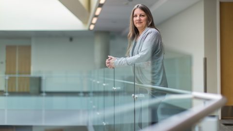 Geralyn Miller rests her arms on a glass rail overlooking a building lobby