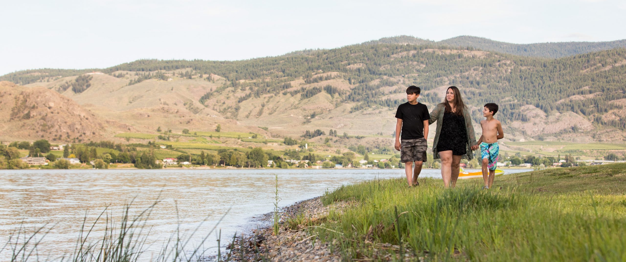 A woman and her two sons walk along the banks of a lake