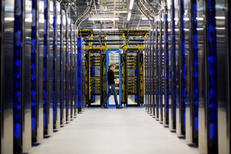 Man walks between stacks of computers at a datacenter