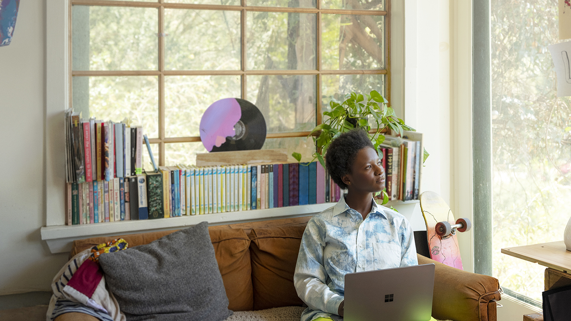 Woman sits on couch with laptop and looks out window