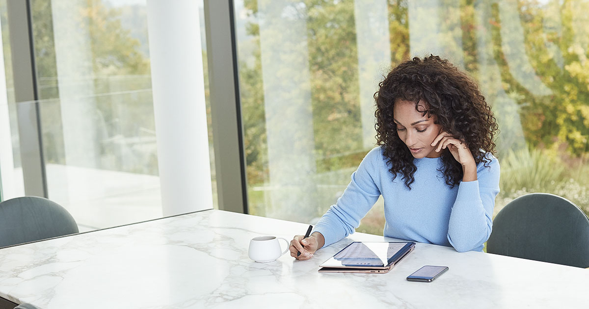 Woman sits at a table with a tablet, her phone, and a beverage cup