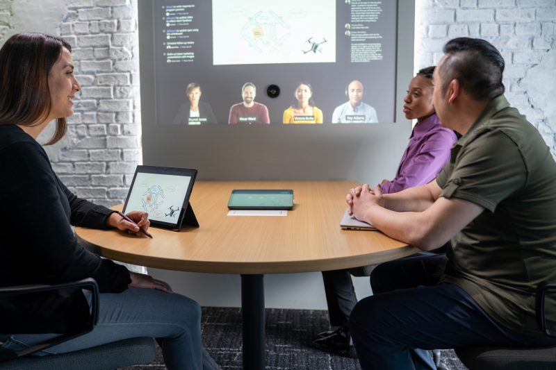 Three meeting attendees talk to colleagues on a screen.