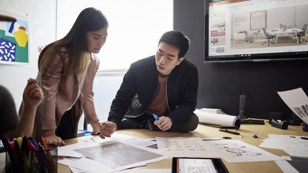 A man and woman collaborate over printed documents, standing over a desk