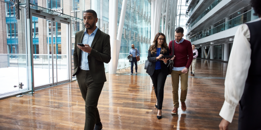 Male and female business professionals walking in large foyer on mobile deivces