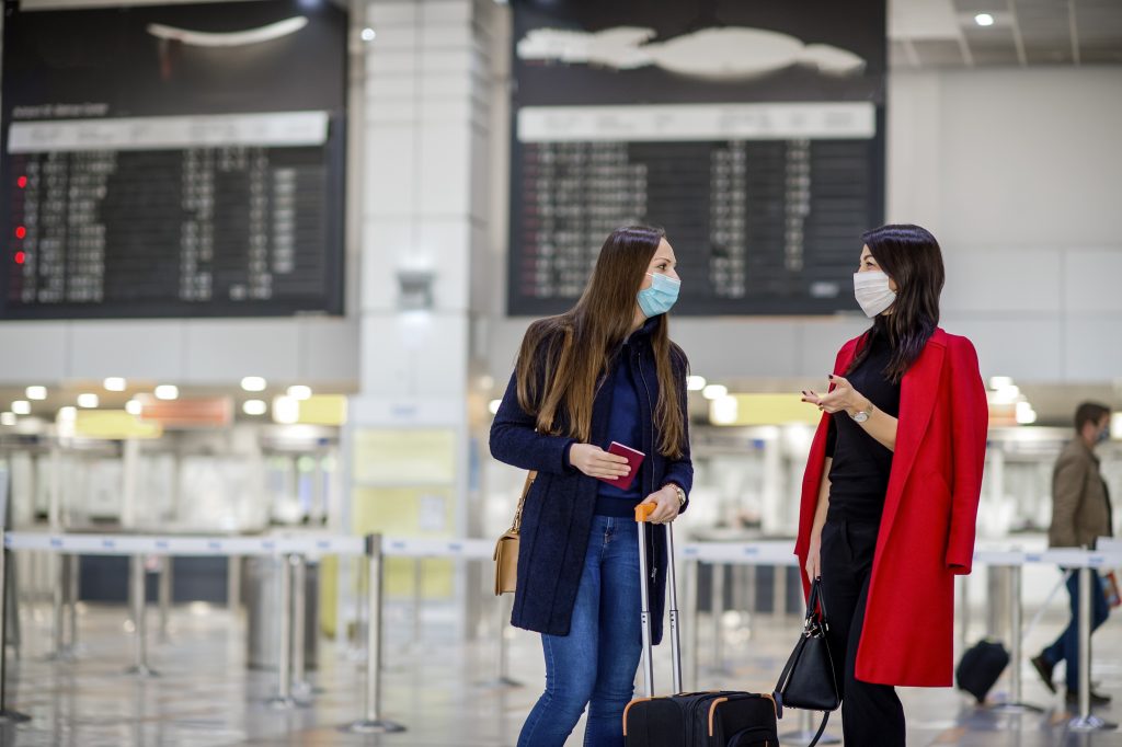 Young business women wearing protective face masks while waiting together in an airport lounge. Travel during pandemic.