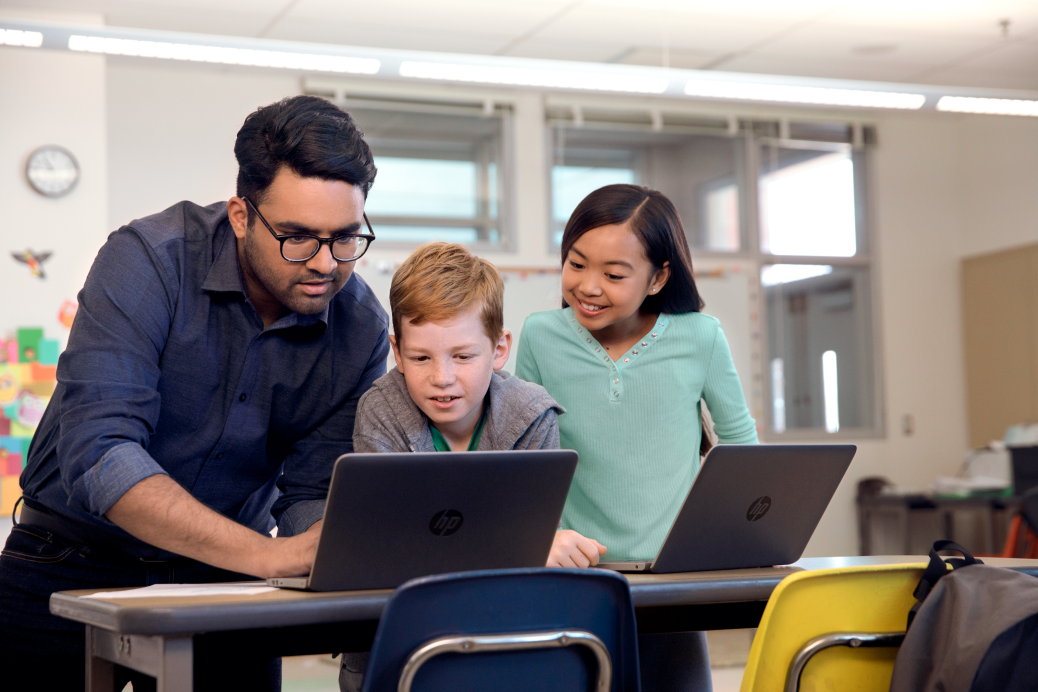 Male teacher assisting two students in a classroom