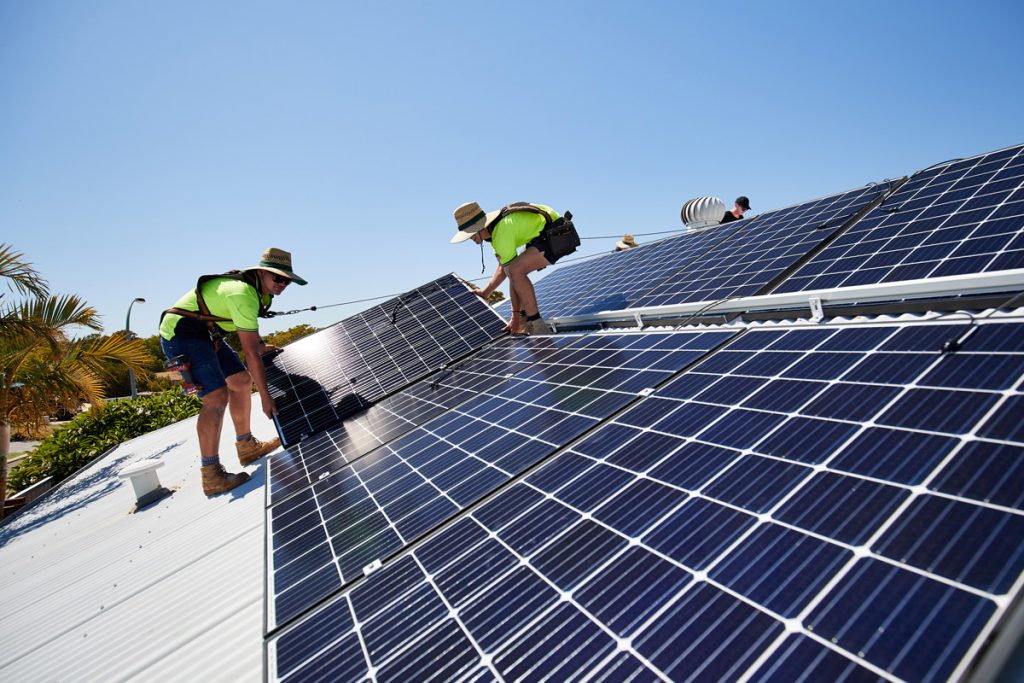 Two male workers in safety gear installing solar roof panels