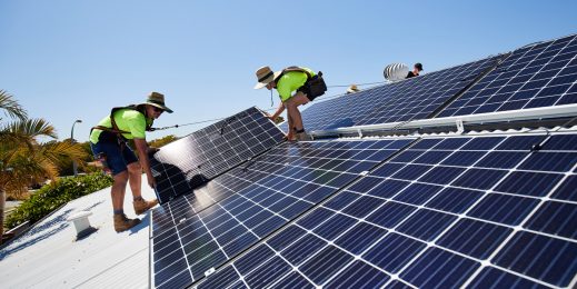 Two male workers in safety gear installing solar roof panels