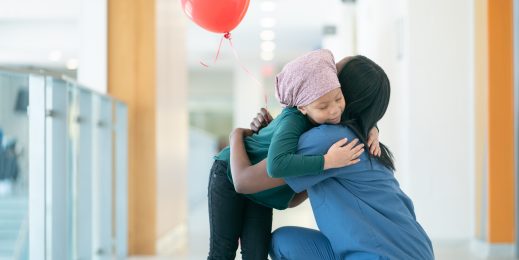 A young female cancer patient wearing a headscarf gives her nurse a big hug as they are both at the hallways at the hospital. She is also holding a red balloon that was gifted to her from the hospital staff.