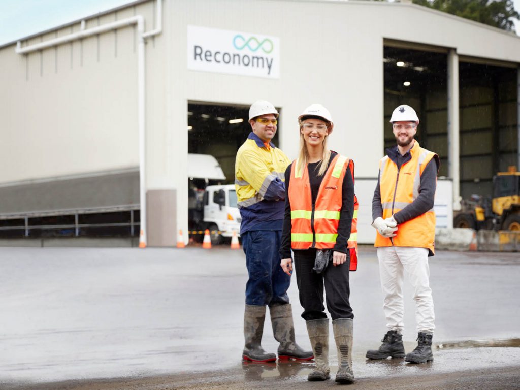 Three adults in safety gear infront of a warehouse building