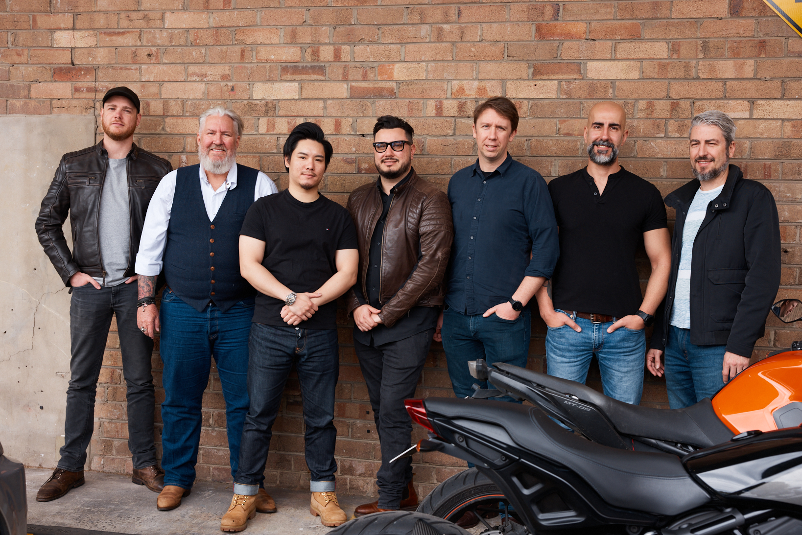 Seven adult males (Forcite team) standing infront of a brick wall