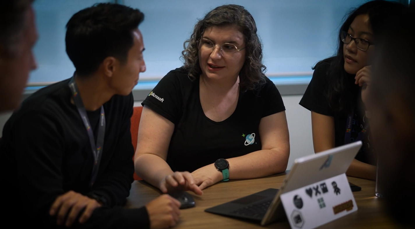 Four adults sitting around a Microsoft Surface laptop