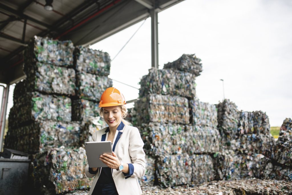 Close-up of female environmental expert using digital tablet for notes while conducting satisfying onsite inspection of recycling facility.