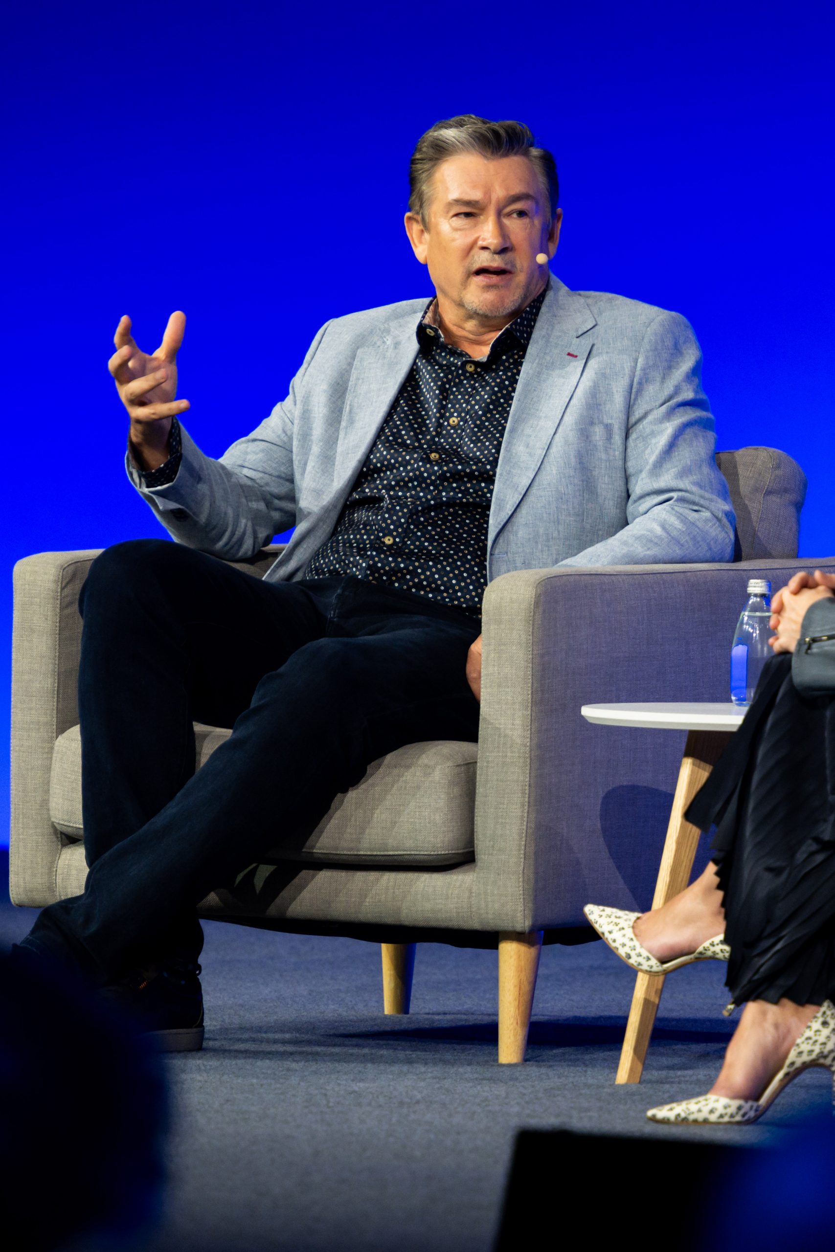 A Caucasian white male seated on a single lounge, speaking to a host beside him