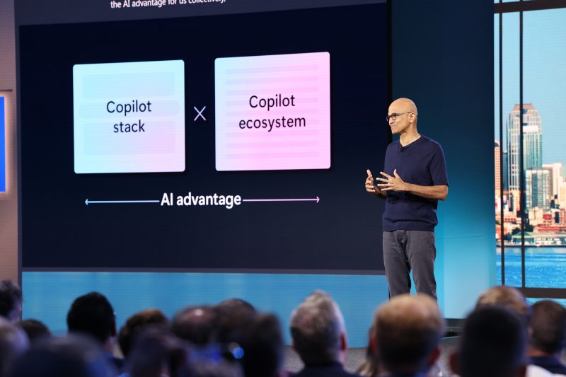 Man stands on stage with technology news projected in the background.