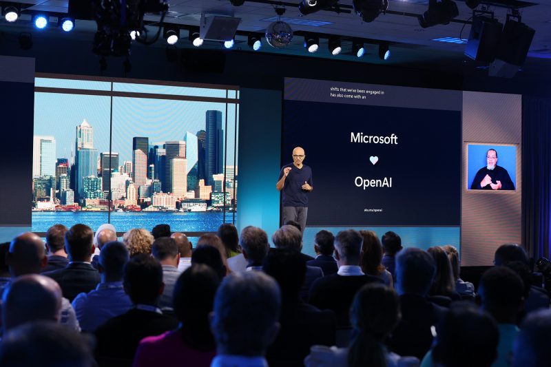 Man stands on stage with technology news projected in the background.