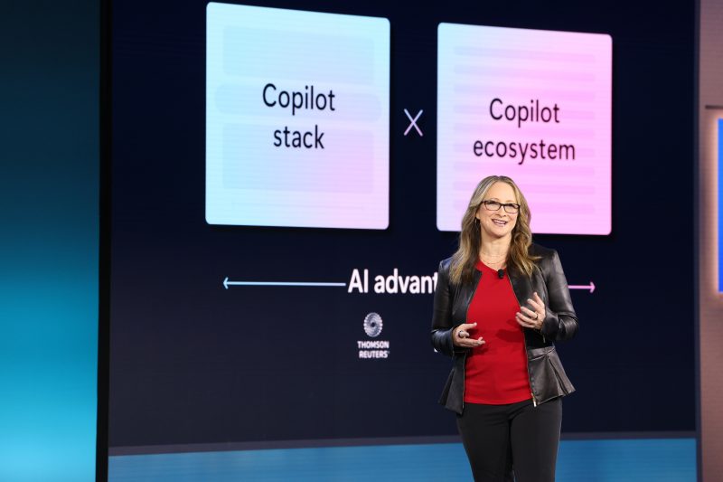 Woman stands on stage with technology news projected in the background.