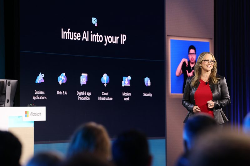 Woman stands on stage with technology news projected in the background.