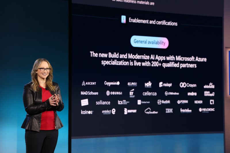 Woman stands on stage with technology news projected in the background.