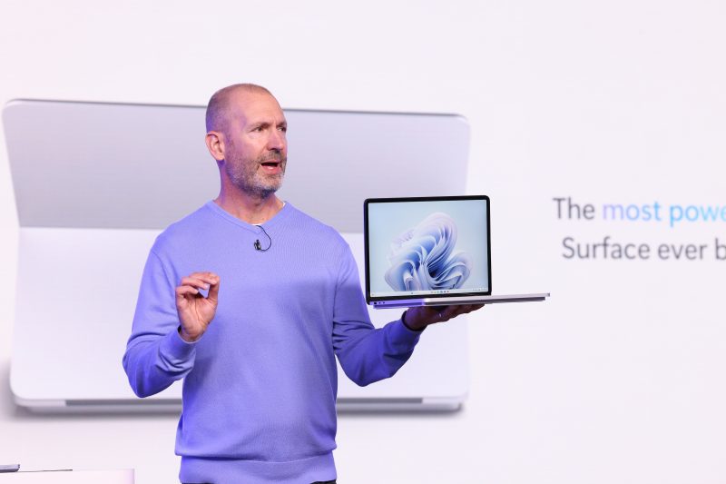 Image of Brett Ostrum, Microsoft corporate vice president for Surface devices, holding a Surface laptop while speaking on stage.