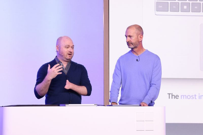 Image of Brett Ostrum, Microsoft corporate vice president for Surface devices, speaking on stage with Solomon Romney, Microsoft accessibility program manager.