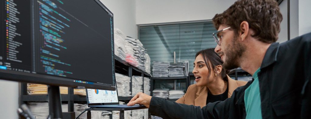 Two people sit in a room working on a laptop.