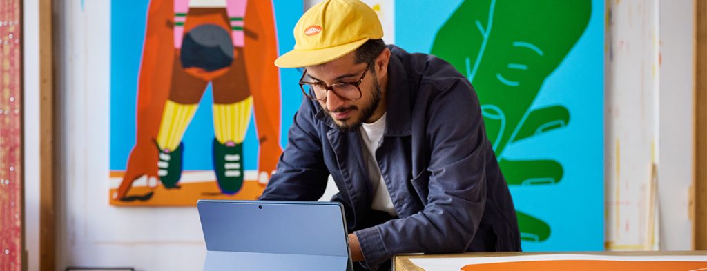 A man sits in front of a colorful mural working on a tablet.